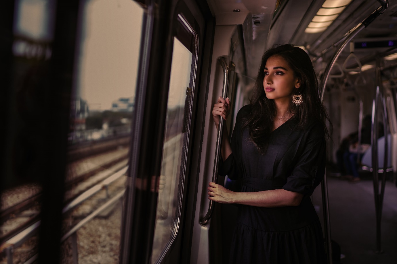 Photo of Woman Standing Inside Train Holding on Metal Rail While Looking Outside